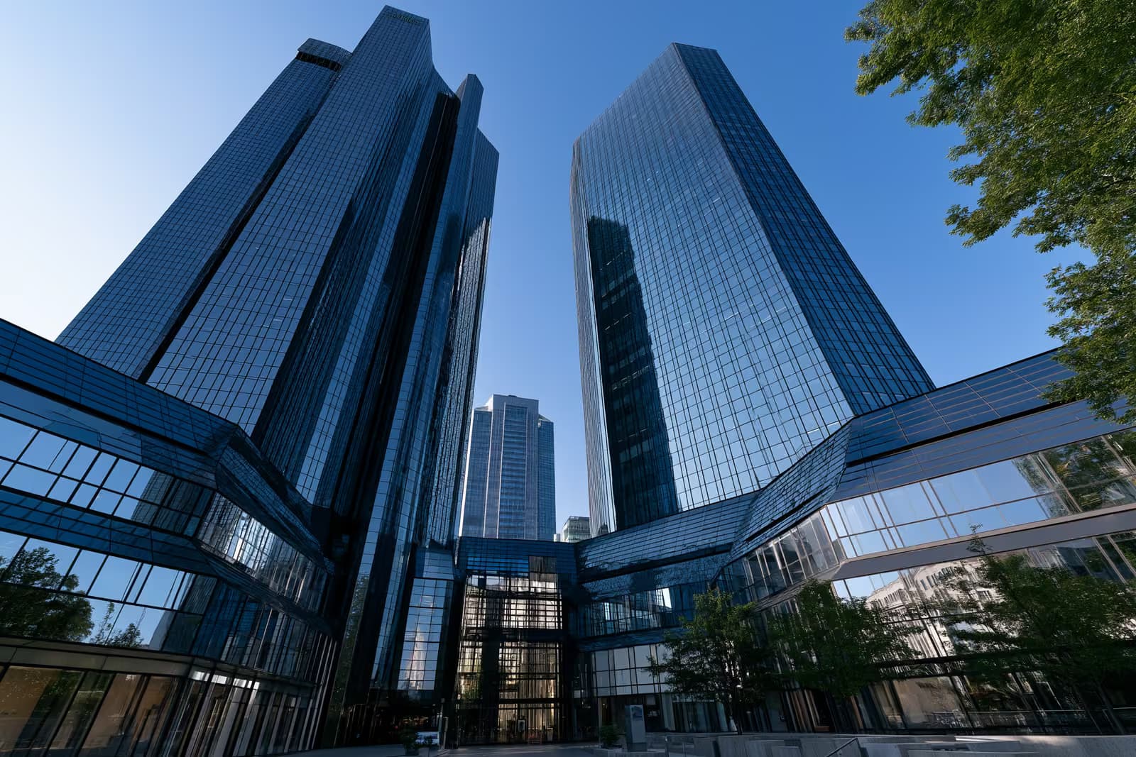 Kulla bankare binjake prej qelqi në Frankfurt që shkëlqejnë kundrejt një qielli blu të ndritshëm, të parë nga poshtë.