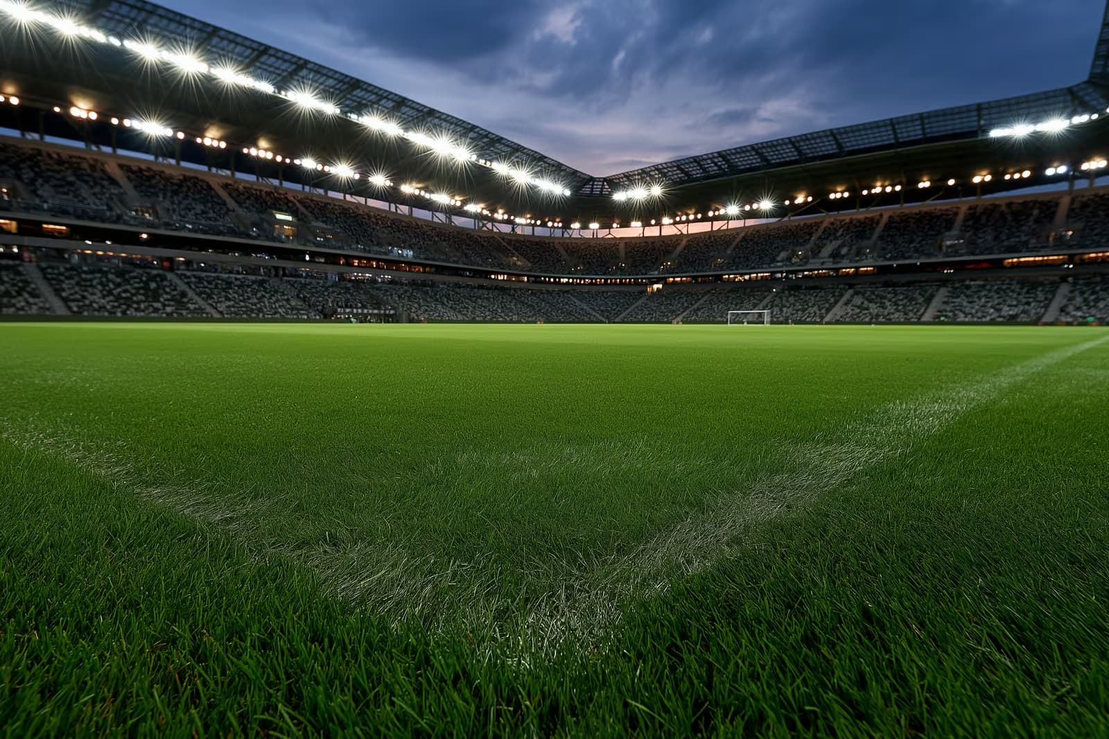 Një stadium futbolli i ndriçuar në muzg para një ndeshjeje në mbrëmje.